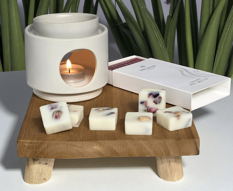White ceramic oil burner with lit candle on a wooden stand, surrounded by decorative wax cubes.